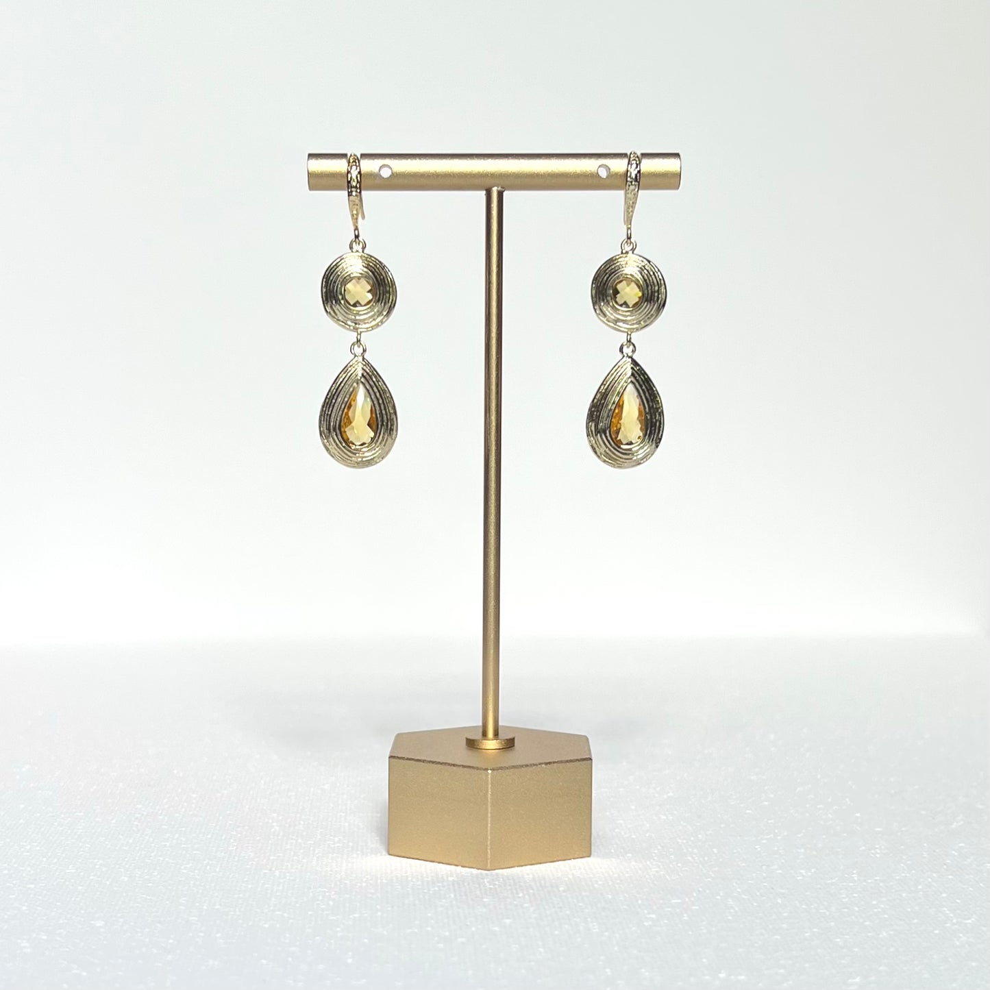 This pair of earrings features a round and teardrop shaped gold charm with citrine color glass centers held by a gold filled French hook.