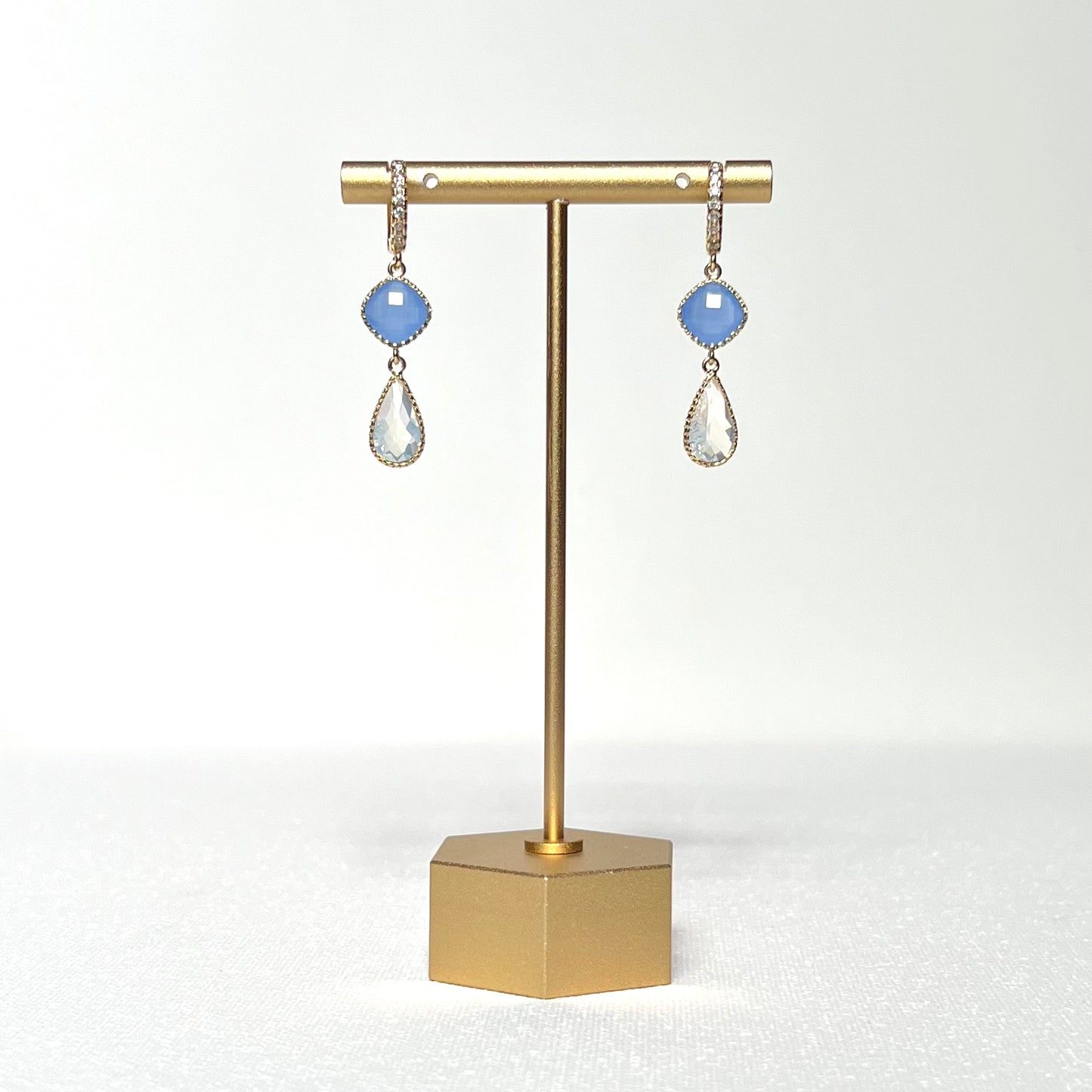This earring set features a blue glass fancy prong set bezel charm with a milky white glass teardrop shaped prong set bezel hung by a gold filled CZ crested huggie style hoop. 