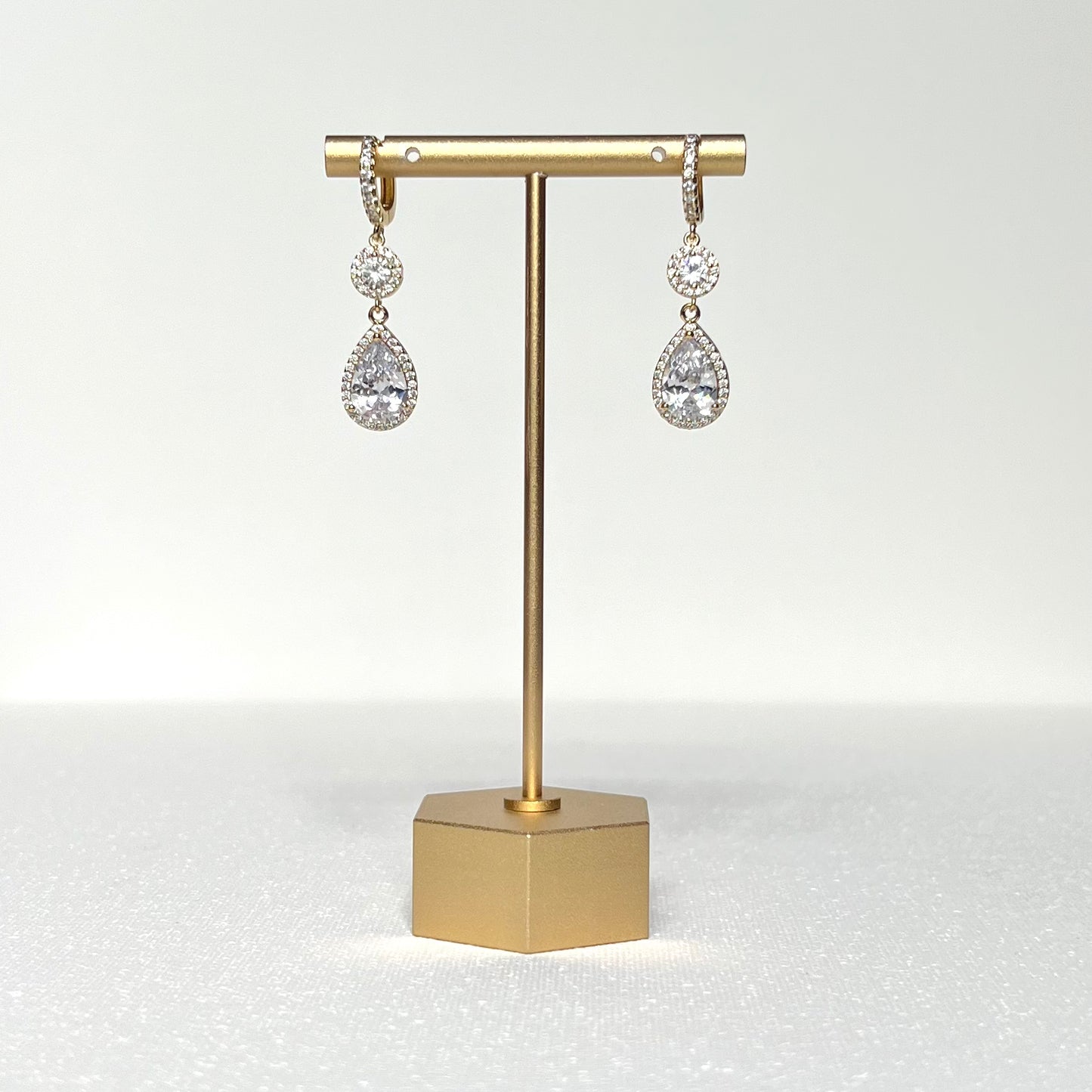 This spectacular earring pair features both a round and teardrop shaped CZ charm in a halo of cubic zirconia, hung on a gold filled CZ crested huggie style earring.